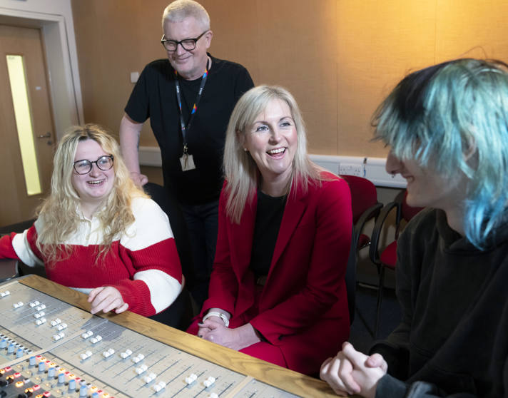 Principal Joanna Campbell chats with students and a staff member in a Glasgow Kelvin College recording studio, all smiling around a sound mixing desk. Principal Joanna Campbell chats with students and a staff member in a Glasgow Kelvin College recording studio, all smiling around a sound mixing desk.